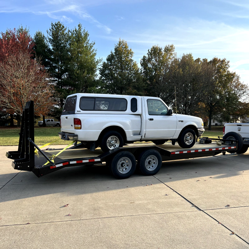 white pickup truck being hauled by trailer